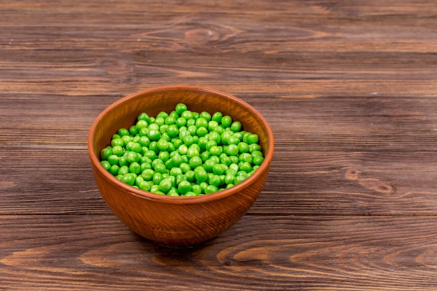 Fresh green peas in a bowl on a brown wooden table