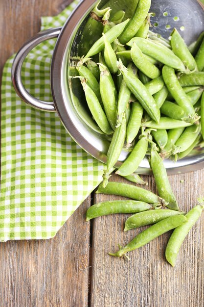 Fresh green peas in colander on wooden background