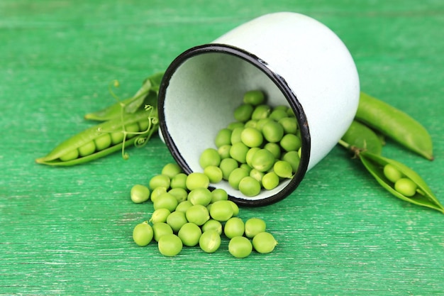 Fresh green peas in metal cup on wooden table
