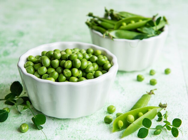 Fresh green peas pods and green peas with sprouts on green wooden background. Concept of healthy eating, fresh vegetables.