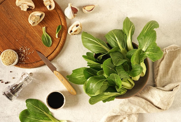 Fresh green pok choy in bowl on gray table and mushrooms on cutting board top view