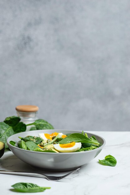 Свежий зеленый салат с яичным авокадо и шпинатом на сером фоне в серой тарелке
