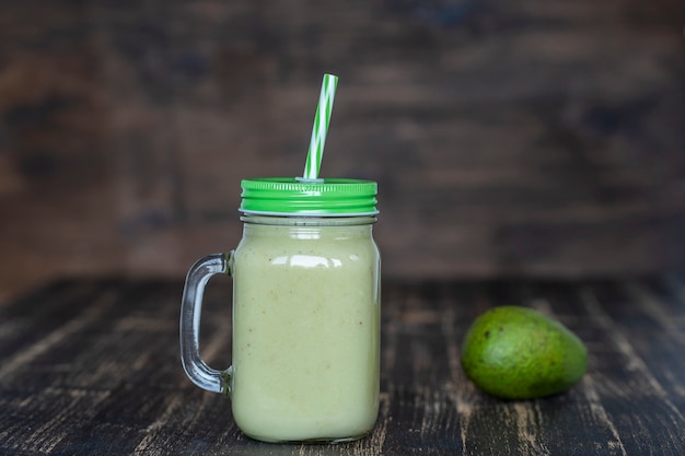 Fresh green smoothie from avocado, banana and honey in glass mug on wooden background, close up. Concept of healthy eating