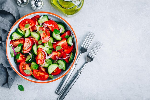 Fresh green summer salad bowl with tomatoes cucumbers red onions basil and olive oil dressing