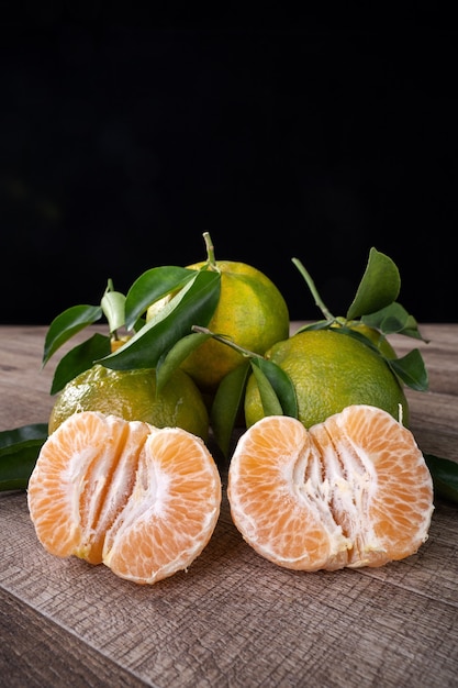 Fresh green tangerine mandarin orange with fresh leaves on dark wooden table background harvest concept.