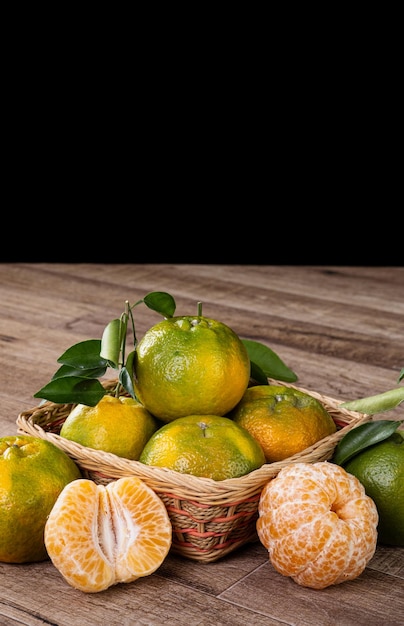 Fresh green tangerine mandarin orange with fresh leaves on dark wooden table with black background harvest concept.