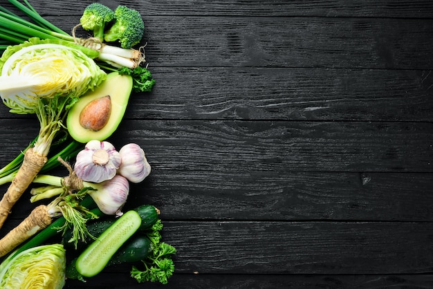 Fresh green vegetables on a black wooden background Avocado cucumber onion garlic Top view Free space for your text