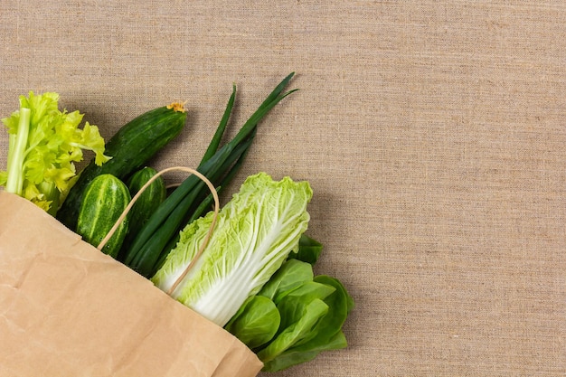 Fresh green vegetables in paper bag on burlap background and copy space