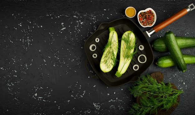 Photo fresh green zucchini in a pan on a dark table. the view from the top. copy space.