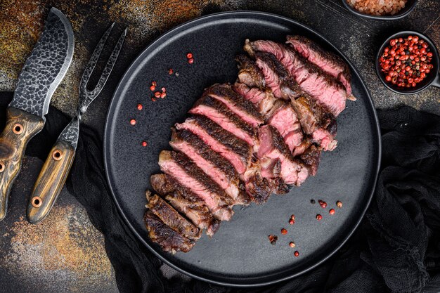 신선한 구운 고기. 구운 소고기 스테이크 미디엄 레어 블랙 앵거스 립아이 스테이크 세트, 접시에, 고기 나이프와 포크, 오래된 어두운 소박한 위에