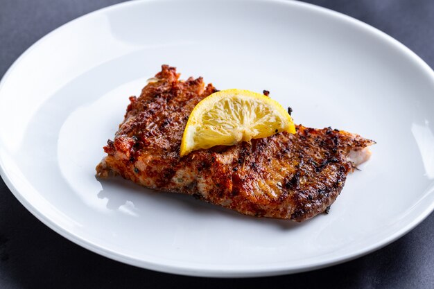 Fresh, grilled salmon fillet with a slice of juicy lemon on a white plate