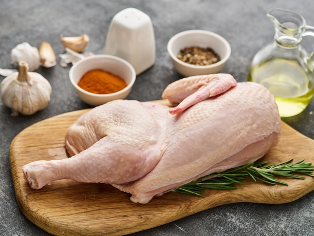 Fresh half of raw chicken with spices and seasonings on a wooden board