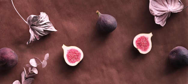 Fresh halved fig fruits and dry euvalyptus and cala lily flowers painted metallic pink on bstract textured background