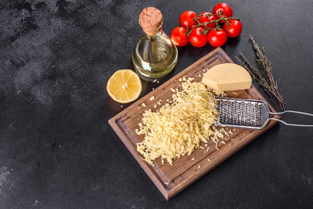 Fresh hard cheese grated on a large grater on a wooden cutting board on a dark concrete background