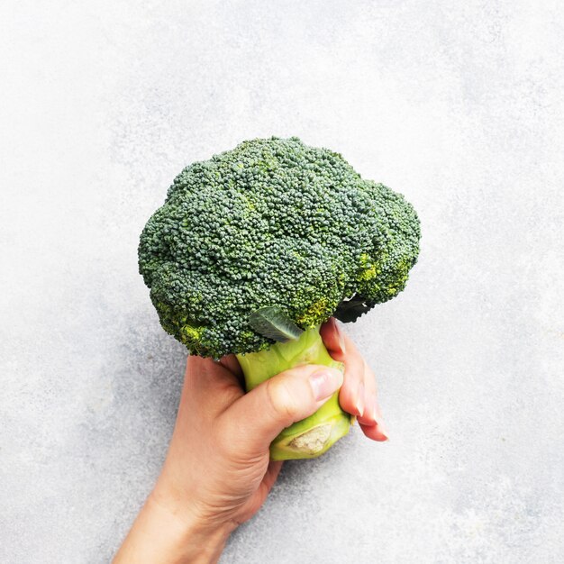 Fresh head of broccoli in a woman's hand on grey concrete table.