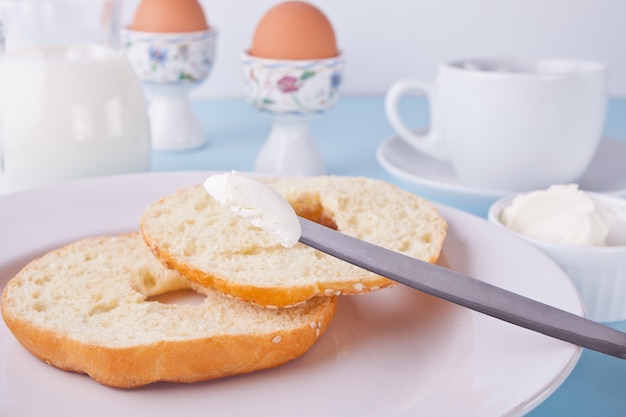Свежий здоровый бублик на белой салфетке с чашкой кофе, сливочным сыром и яйцами на завтрак.
