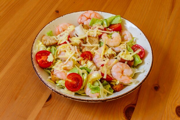 Fresh healthy caesar salad with prawns cherry tomatoes lettuce parmesan cheese dressing and croutons on wooden table