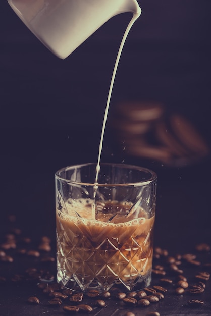 Latte fresco e sano che versa dalla brocca in un bicchiere di latte freddo e biscotti al caffè al cioccolato.