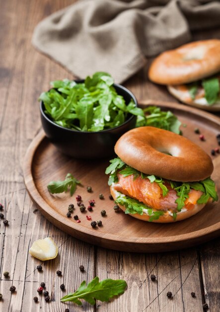 Fresh healthy organic sandwich with bagel and salmon cream cheese and wild rocket in bowl plate on wooden table background with towel