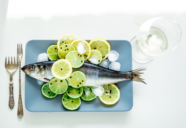 Fresh herring fish with lemons and peppers and wineglass on white surface. Above view