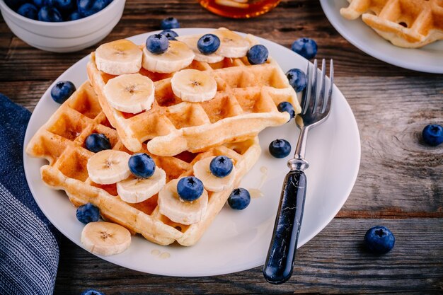 Fresh homemade belgian waffles with blueberries and banana for breakfast on wooden background