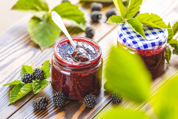 Fresh homemade blackberry jam in glass jar on a wooden background Several fresh berries are near it