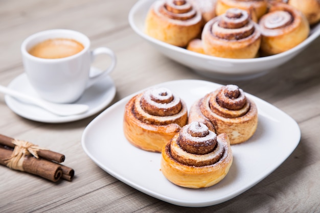 Fresh homemade buns with cinnamon, a cup of coffee, cinnamon sticks. Selective focus, close-up