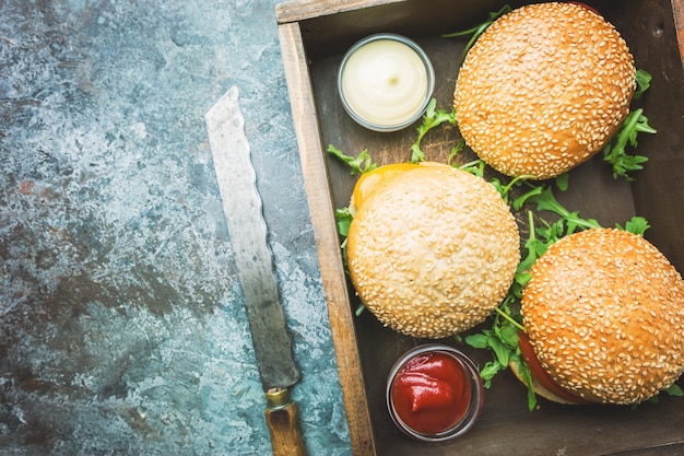 Fresh homemade burger in a box with spicy sauce and herbs over dark stone background. Top view with copy space