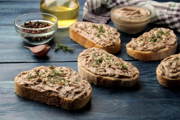 Fresh homemade chicken liver pate with herbs on bread on a blue wooden table. A sandwich.