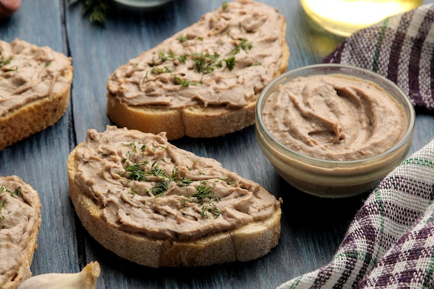 Fresh homemade chicken liver pate with herbs on bread on a blue wooden table. A sandwich.