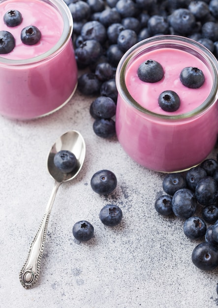 Fresh homemade creamy blueberry yoghurt with fresh blueberries and silver spoon on stone table