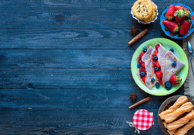 Fresh homemade crepes served on a plate with strawberries and blueberries, on a dark wooden background,