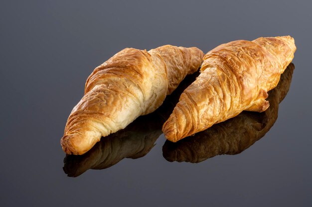 Fresh homemade croissant on black reflective background.