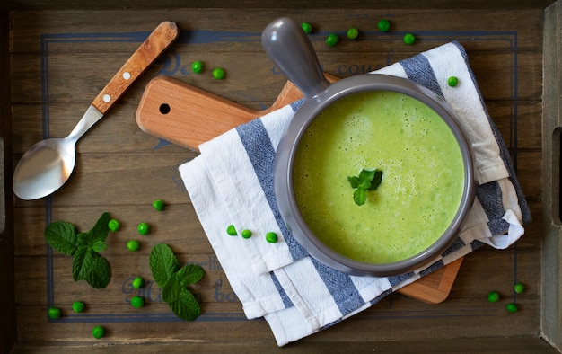 fresh homemade diet cream soup of green peas and broccoli served with mint on a dark wooden tray. top view