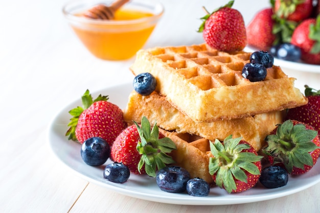 Fresh homemade food of berry Belgian waffles with honey, chocolate, strawberry, blueberry, maple syrup and cream. Healthy dessert breakfast concept with juice