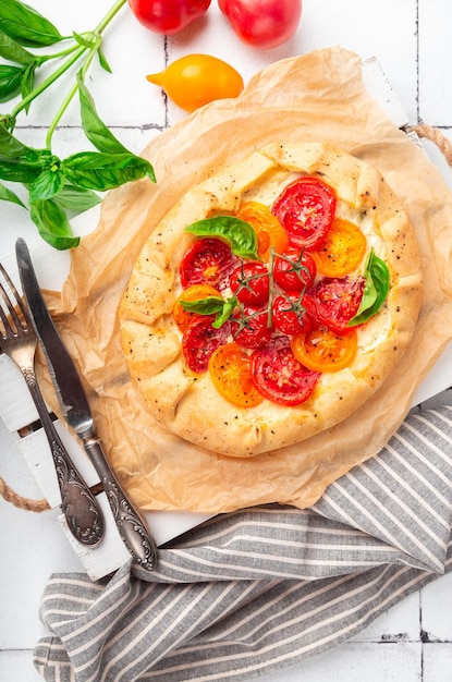 Foto galette fresca fatta in casa con pomodori, ricotta e basilico su sfondo di piastrelle bianche vista dall'alto