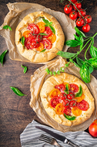 Galette fresche fatte in casa con pomodori, ricotta e basilico su fondo rustico di compensato