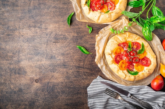 Fresh homemade galettes with tomatoes ricotta cheese and basil on rustic plywood background