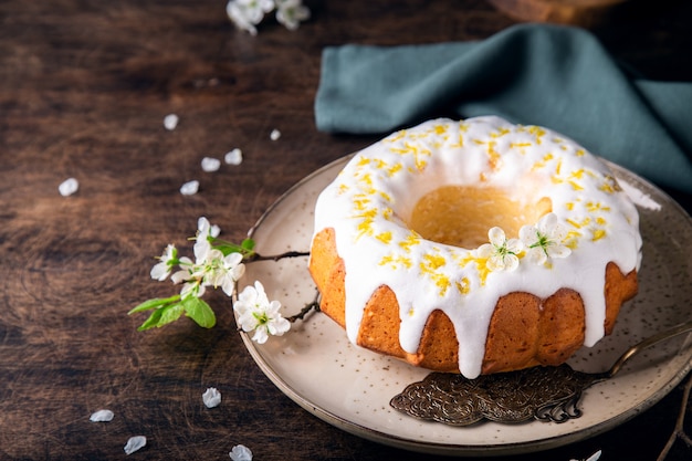 fresh homemade lemon bundt cake decorated with white glaze and zest on rustic wooden background