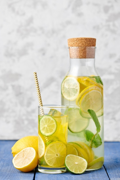 Foto limonata fresca fatta in casa con lime e menta nel bicchiere con carta paglia e bottiglia su sfondo blu brillante