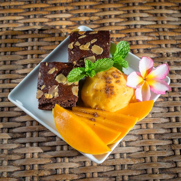 木のテーブルにミントの葉とチョコレートブラウニーを添えた新鮮な自家製有機マンゴーアイスクリームシャーベットをタイの接写