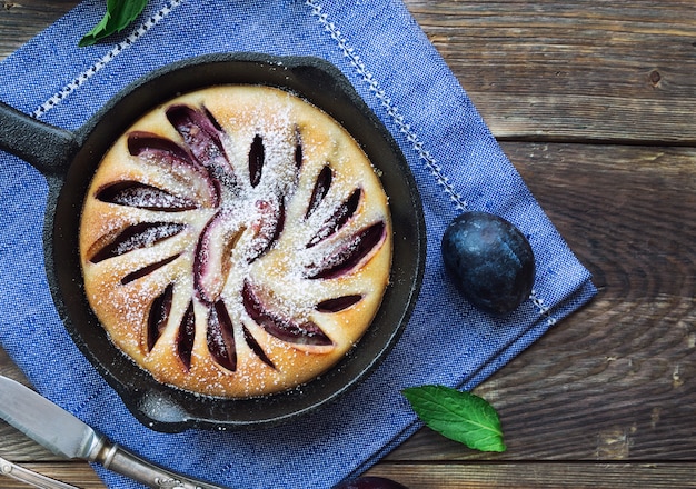 Fresh homemade plum cake in iron skillet on rustic wooden table. Top view.