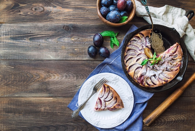 Fresh homemade plum clafoutis made in iron skillet on rustic wooden background. Top view. Copy space area.