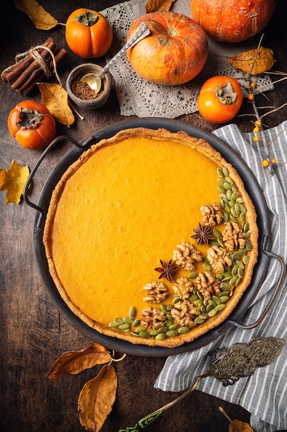 Fresh homemade pumpkin pie for Thanksgiving decorated with walnuts and seeds at vintage tray on rustic plywood background. Top view.