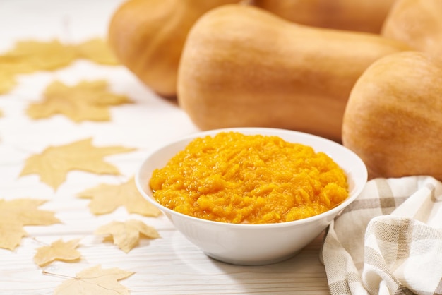 Fresh homemade pumpkin puree in bowl on a white wooden table yellow autumn leaves in back