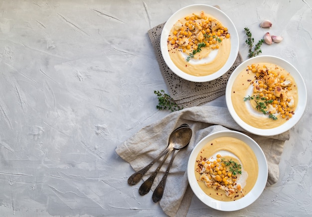 Fresh homemade roasted cauliflower and chickpea soup in bowls on light gray concrete background