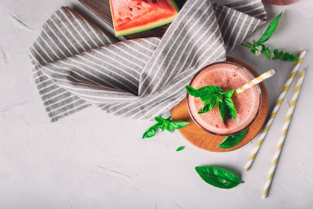Fresh homemade watermelon and basil smoothie in glass on white concrete background