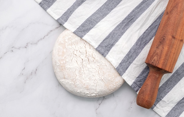 Fresh homemade yeast dough resting on marble table with rolling pin flat lay.