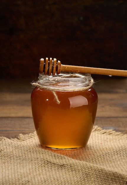 Fresh honey in a transparent glass jar and a wooden spoon on a brown table