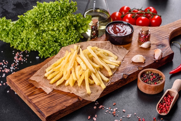 Fresh hot french fries with salt vegetables and spices on a dark concrete background